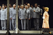 Die Oper „Fidelio“ hat eine besondere Bedeutung in der Geschichte der Semperoper und ihres Chores: Die erste Oper, die nach dem Zweiten Weltkrieg, erst nur konzertant, später auch szenisch wieder gespielt wurde, erlebte ihre Premiere in der Inszenierung von Christine Mielitz 1989. Anlässlich des 25. Jahrestags der Wiedervereinigung im Jahr 2015 erinnerte sich die ehemalige VdO-Vorsitzende und Sängerin im Opernchor der Sächsischen Staatsoper, Margot Ehrlich: „Premiere war am 7. Oktober, am Tag der Republik, an dem die Politik noch, die Zeichen der Zeit missachtend, sich selbst und 40 Jahre DDR feierte. ‚Fidelio‘ in Dresden zeigte ein anderes Bild. Der Gefangenenchor spielte sich hinter Stacheldraht ab. Diese Inszenierung war für uns alle auch bedrückend… Der Stacheldraht ging nicht zu den Gefangenen auf der Bühne, sondern eigentlich zum Publikum, diente also nicht dazu, das Publikum vor den Gefangenen zu schützen, sondern eher umgekehrt.“ (O&T, 6/2015). Das Foto (Matthias Creutziger) zeigt Ute Selbig als Marzelline und Herren des Sächsischen Staatsopernchors.